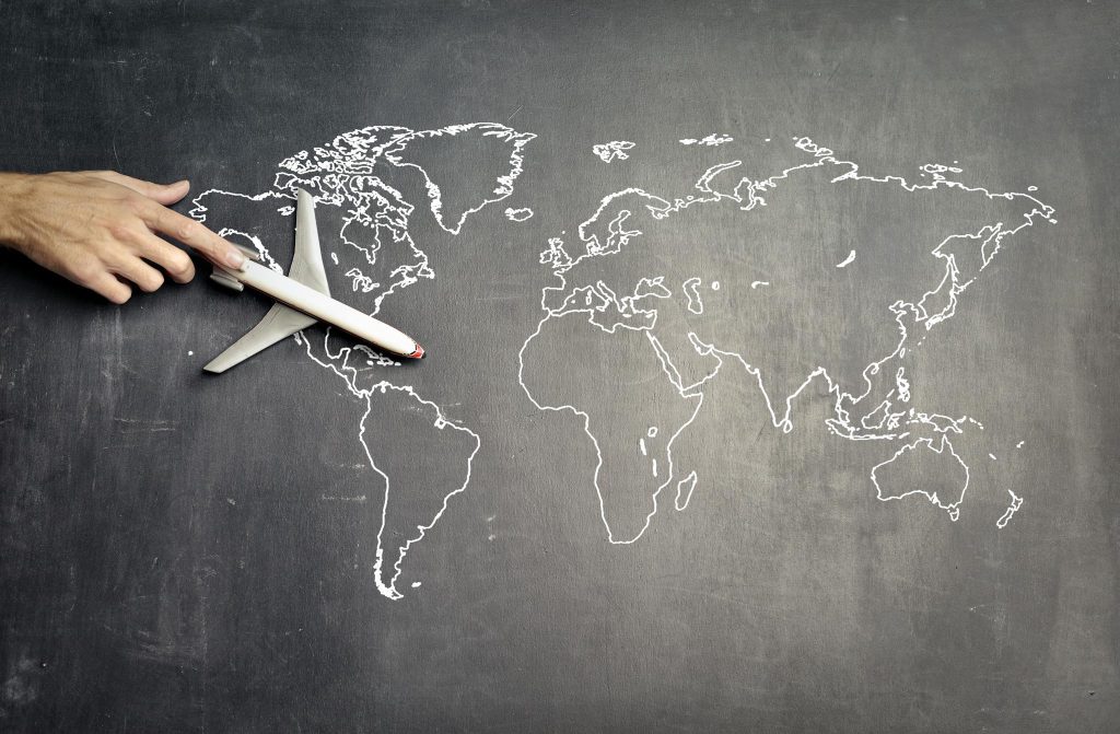 From above: a toy airplane on empty world map drawn in white chalk on blackboard