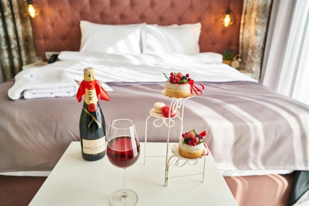 Photo of Wine Bottle And Food On Table in front of made bed